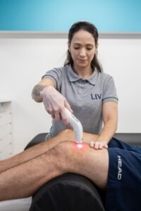 Fisioterapeuta do LIV aplicando laser no joelho de um paciente durante a Fisioterapia